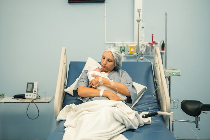 New mother resting in hospital bed, holding newborn baby, reflecting on quiet down and stop screaming after birth.