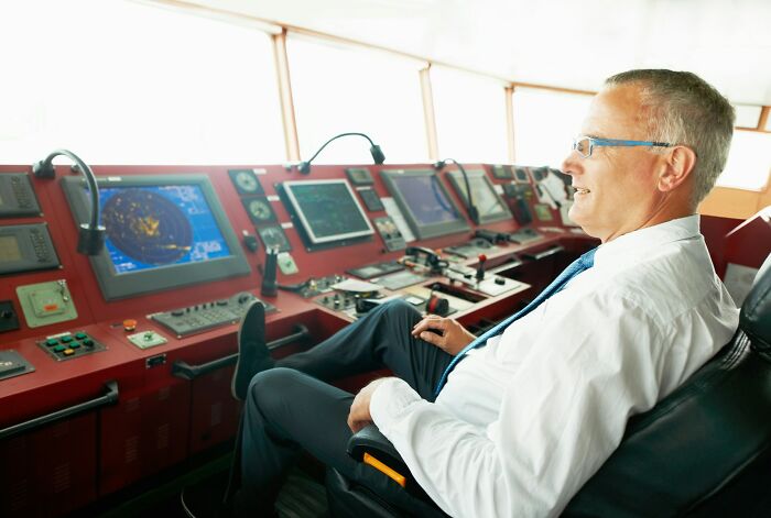 Experienced man in a white shirt and glasses operating navigation controls on a ship, illustrating high-paying jobs concept.