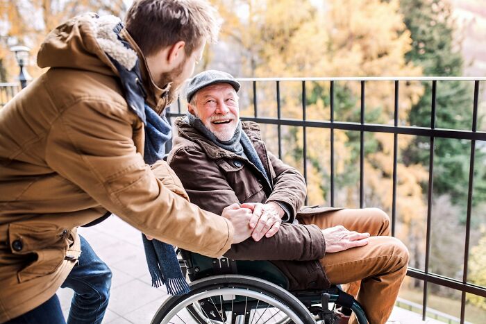 Older man in wheelchair sharing a joyful moment outdoors with younger man, illustrating life after divorce for older people. - 27