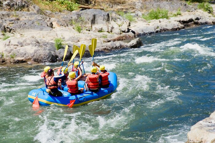 Group of people wearing helmets and life jackets rafting on rapids, sharing hard-to-believe stories about themselves.