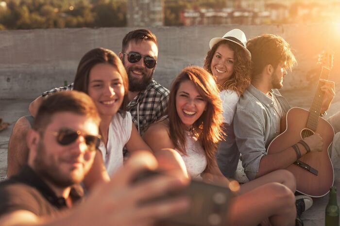 Group of friends smiling and taking a selfie outdoors at sunset, enjoying music and relaxed social time together.
