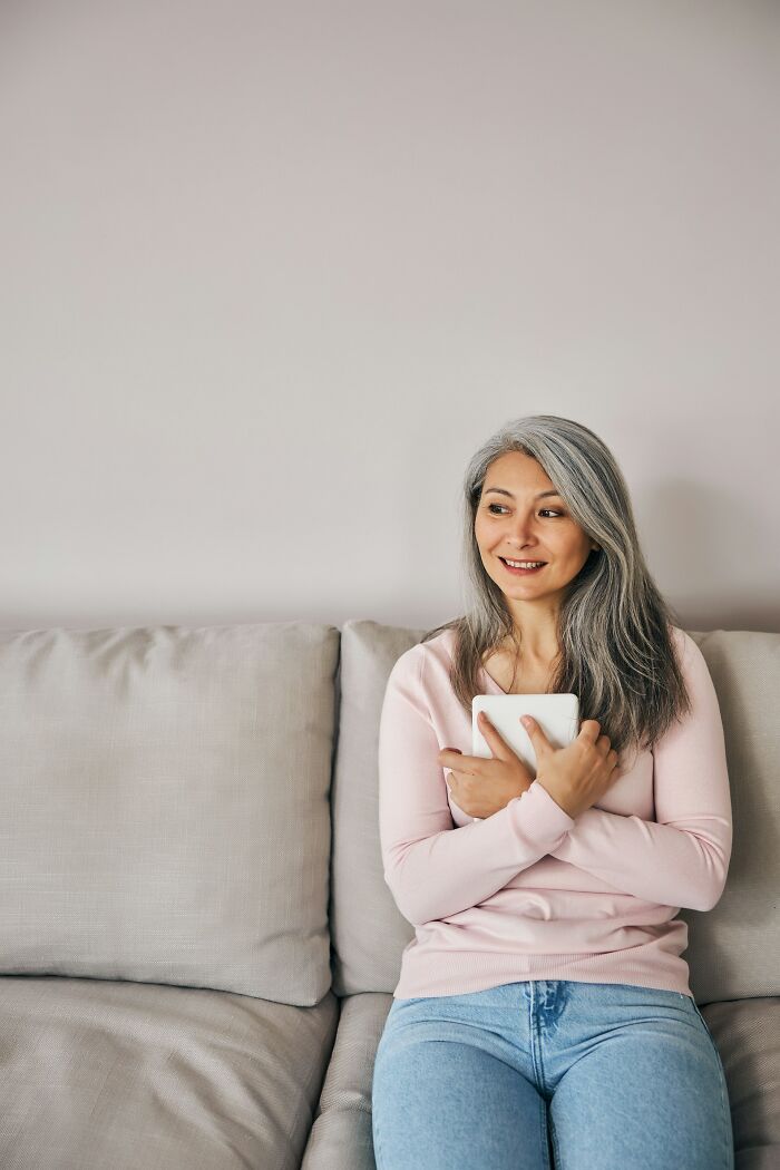 Older woman with gray hair sitting on a couch holding a tablet, reflecting on life after divorce. - 19