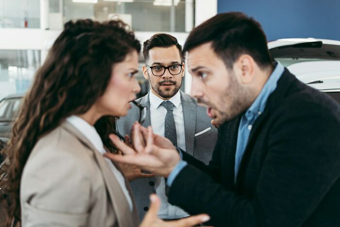 Two adults arguing intensely while a man in a suit observes, highlighting the challenge of communicating calmly in stressful situations.