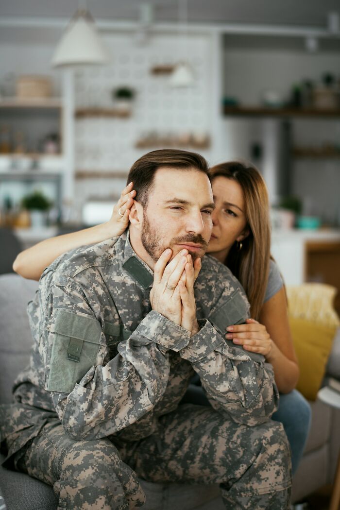 Worried man in military uniform sitting on couch while woman comforts him, illustrating parents punishing their kids too far