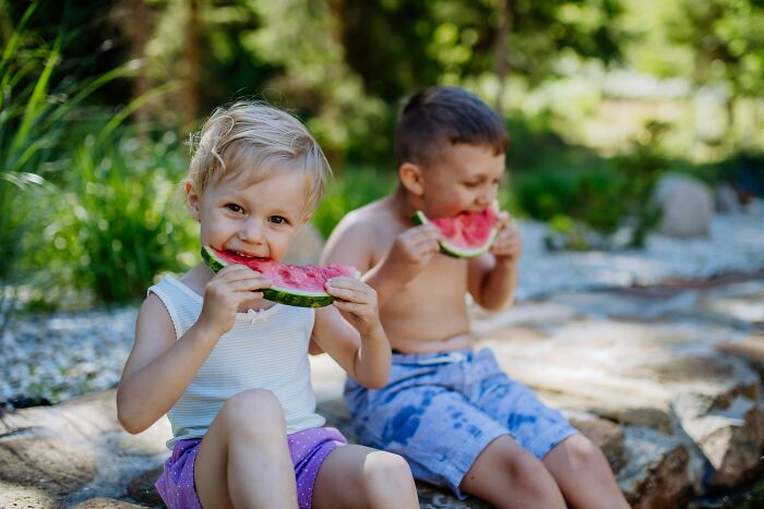 Two children sitting outdoors enjoying watermelon slices, illustrating side effects eating watermelon in a natural setting. - 2