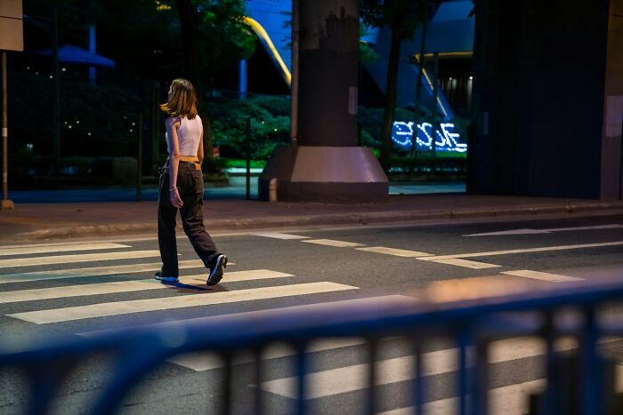 Woman walking alone at night on a city crosswalk, illustrating things men find normal but seem bizarre to women.