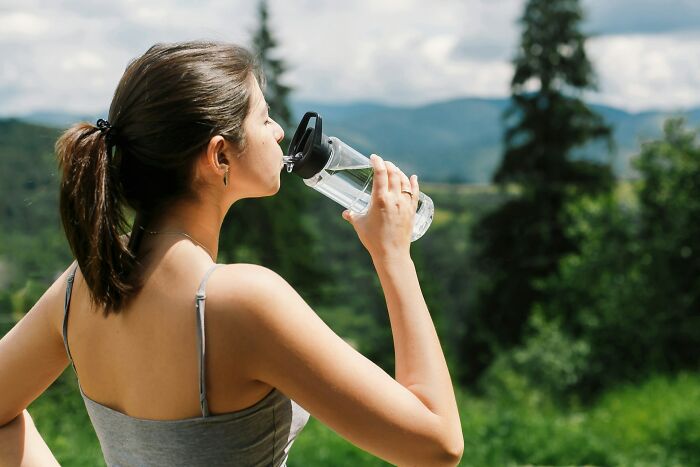 Woman drinking water outdoors surrounded by nature, illustrating mysterious body quirks related to health and hydration.