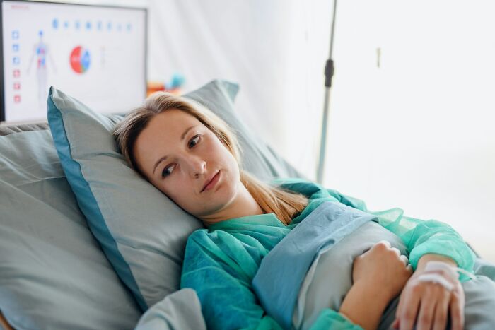 Woman in hospital bed looking tired and reflective, representing the challenges women face after birth.