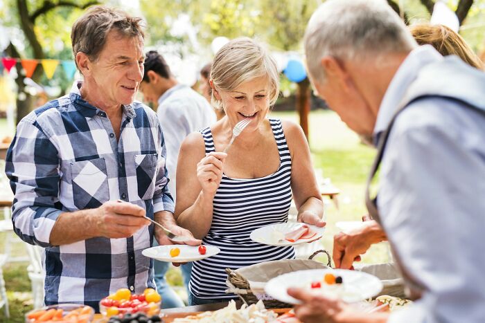 Group of middle-aged people enjoying outdoor party, serving food and smiling, reflecting moments of arrogant people regret.