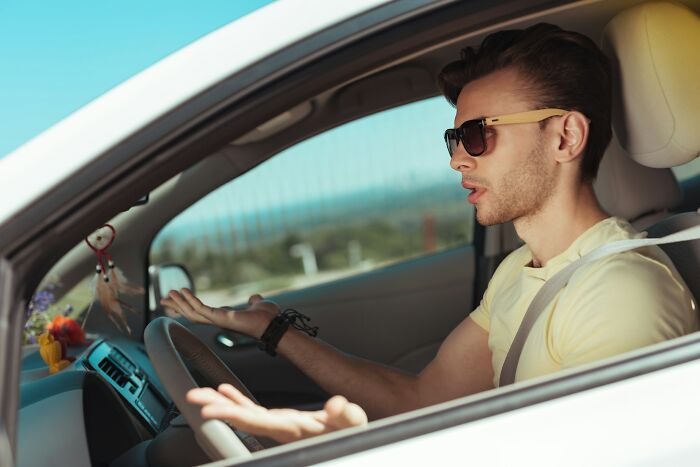 Man wearing sunglasses in car seatbelted, gesturing with hands showing frustration, reflecting what makes a man instantly unattractive to women
