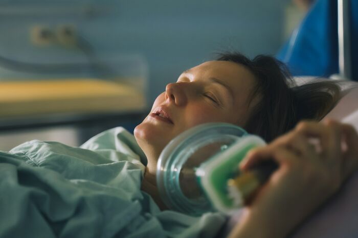 Woman in a hospital bed holding an oxygen mask, representing women sharing awful things they were told after birth.