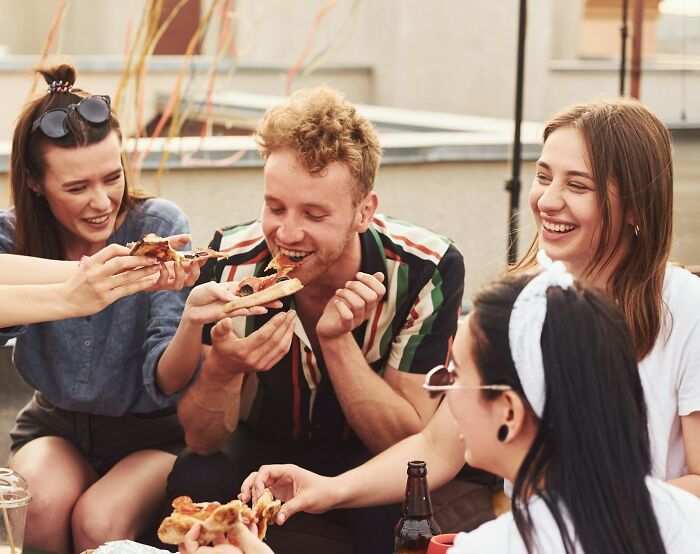 Group of friends laughing and sharing pizza, illustrating moments before discussing partner shenanigans and relationship challenges.