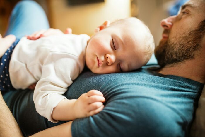 A sleeping baby resting on a man's chest, symbolizing small daily wins from feminists in everyday life.