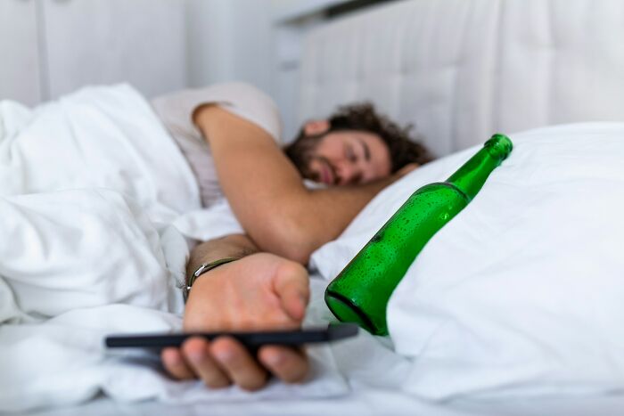 Man lying in bed with a beer bottle and phone, illustrating themes from people who ran away from home stories. - 21