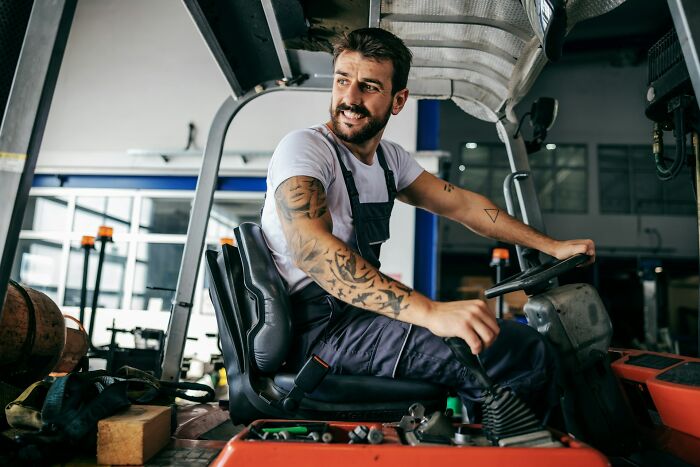 Man with tattoos driving forklift in industrial warehouse, highlighting concerns about things on the brink of collapse. - 14