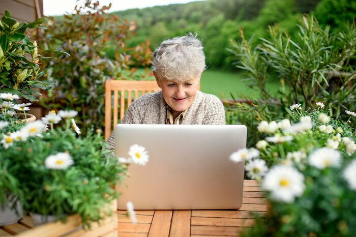 Elderly woman using laptop outdoors surrounded by flowers, representing people who know pathological liars.