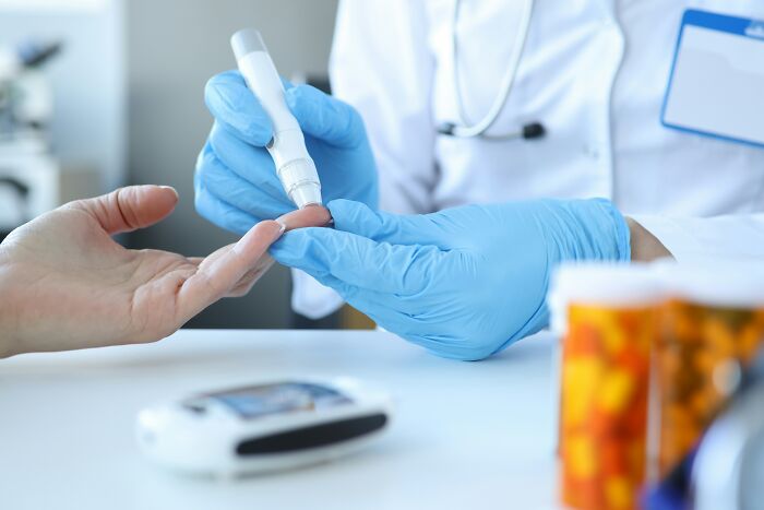 Healthcare professional wearing blue gloves checking blood sugar levels on a patient's finger, illustrating side effects eating watermelon. - 4