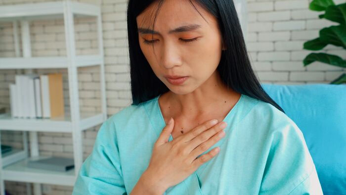 Woman in a turquoise shirt holding her chest with a pained expression, illustrating side effects of eating watermelon. - 3