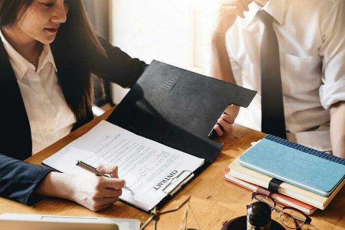Woman in business attire reviewing and signing a contract, illustrating daily wins from feminists in a professional setting.