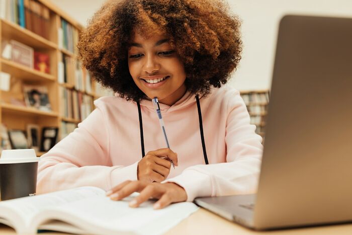 Young woman studying at a desk with a laptop and book, representing small daily wins from feminists.