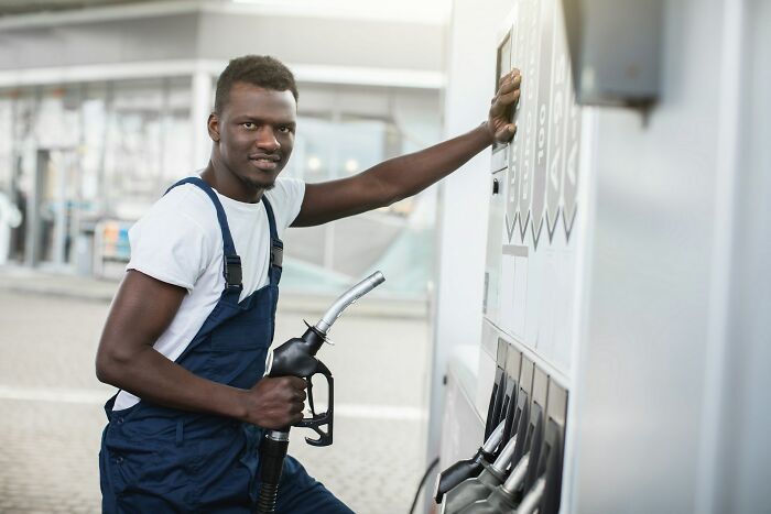 Young man in overalls holding gas pump at fuel station, symbolizing stories from people who know pathological liars.