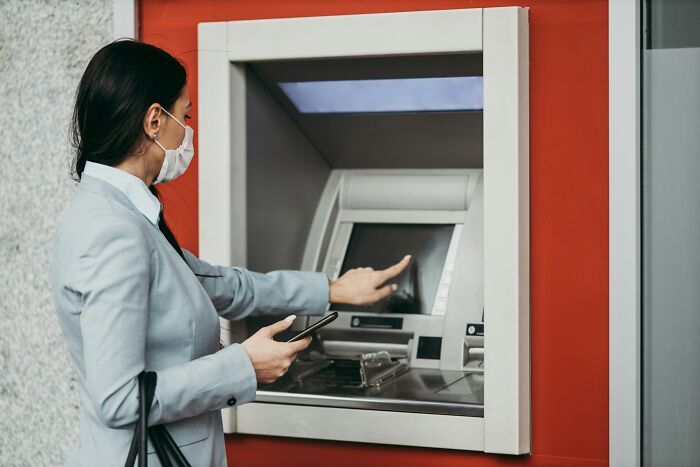 Woman using ATM machine outside wearing a mask, illustrating things non-Americans do that confuse Americans. - 33