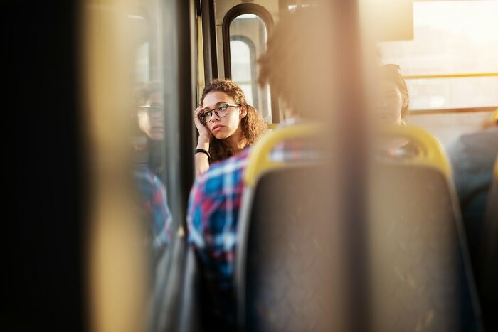 Young woman with glasses looking thoughtful and reflective, sharing hard-to-believe stories about herself on a bus.