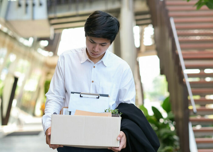Young man holding box of personal items, looking down after leaving office, illustrating stories of revenge on their bosses. - 12