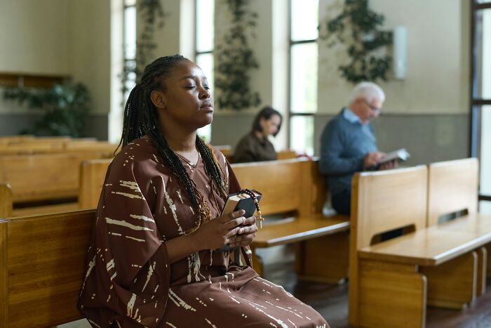 Woman praying with rosary beads in church pews, reflecting on common religious myths about Jesus and the Bible.