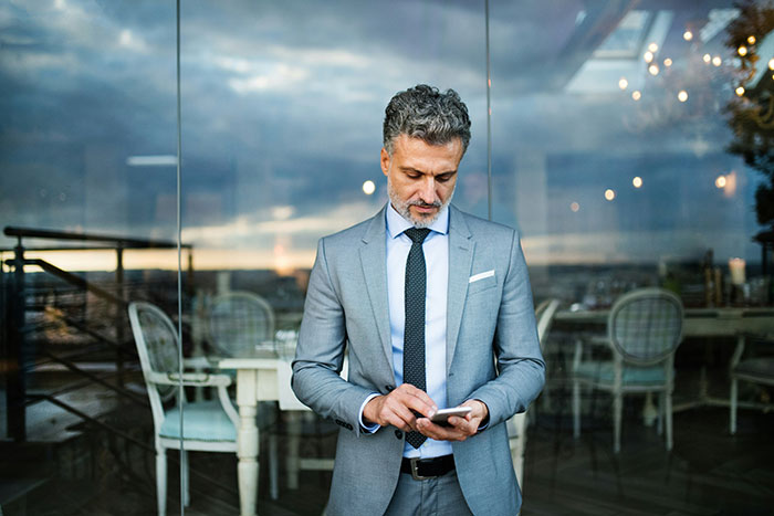 Man in a gray suit looking at his phone outside a cafe, reflecting on fiancee leaving after cancer diagnosis partner news. - 38
