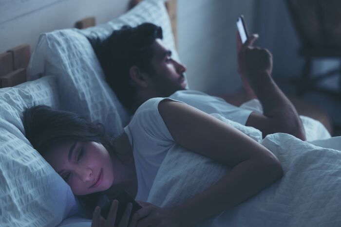 Couple lying in bed at night using smartphones, illustrating the theme of outrageous student names revealed by a teacher.