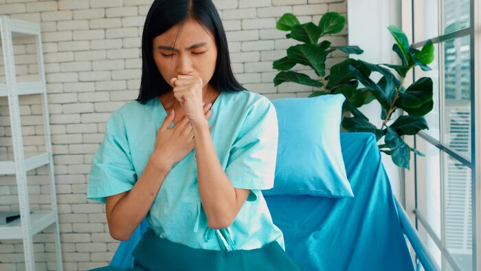 Young female patient coughing while sitting on hospital bed, illustrating impostor patients needing less meds and common sense.