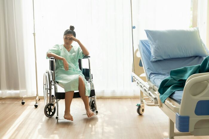Woman in hospital gown sitting in a wheelchair looking distressed after birth, highlighting awful things told to women postpartum