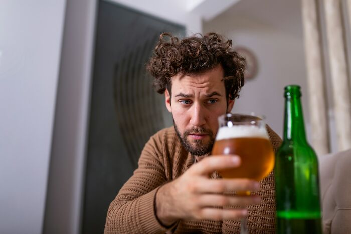 Young man with curly hair holding a beer glass, looking troubled, representing messed up school incidents theme. - 35