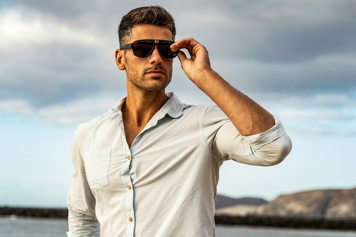 Man wearing sunglasses and white shirt outdoors by the sea, representing traits that make a man instantly unattractive.