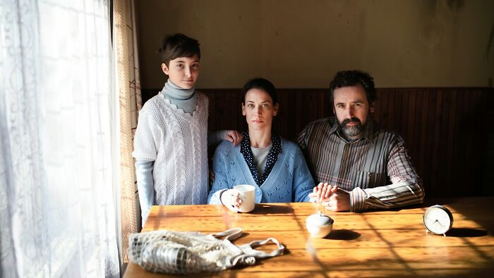 Family sitting solemnly at a wooden table, illustrating parents punishing their kids in extreme ways.