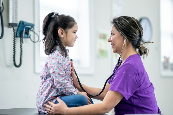 Female doctor using stethoscope to check young girl’s health, representing daily wins for feminists in healthcare.