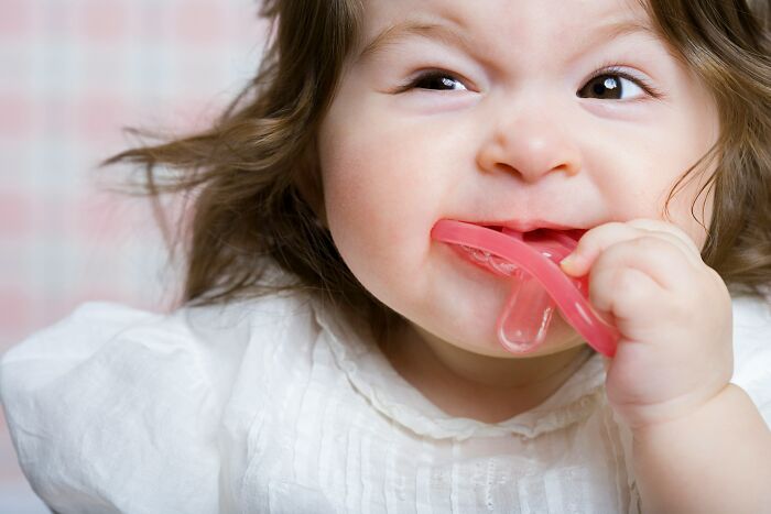 Baby chewing on a red teething toy, illustrating bizarre beliefs people still fall for despite science busting myths. - 17