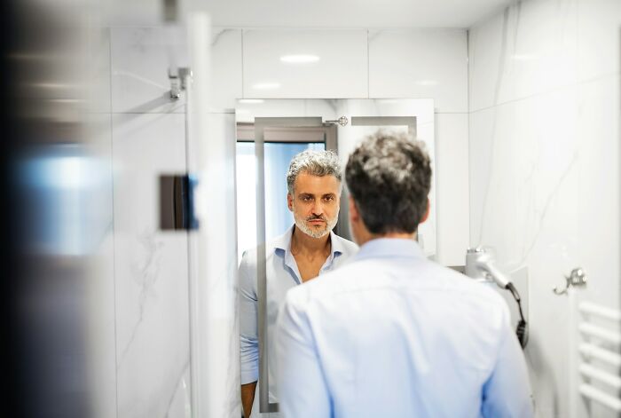 Middle-aged man looking at his reflection in a bathroom mirror, illustrating what makes a man instantly unattractive to women.