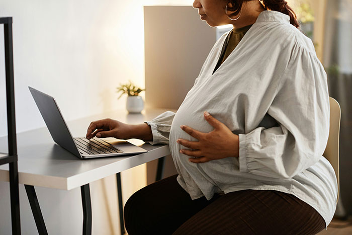 Pregnant woman working on laptop at home, reflecting family conflict and racist switch over babysitting niblings.