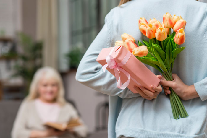 Person hiding a gift and flowers behind their back, preparing a Mother's Day surprise for a girlfriend's mom. - 1