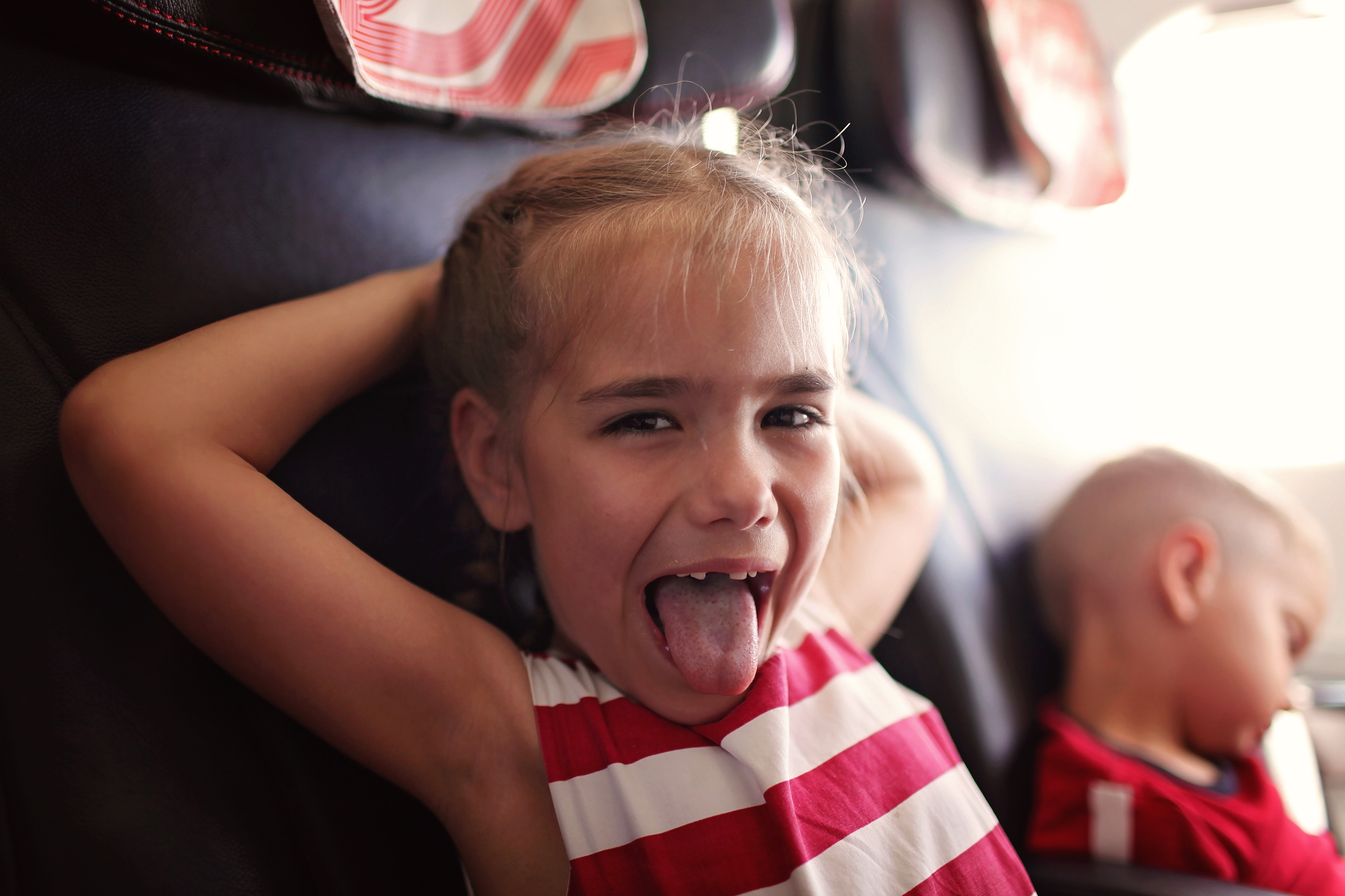 Child making a playful face on airplane seat while another child sleeps, illustrating rowdy kids during flight situation. - 5