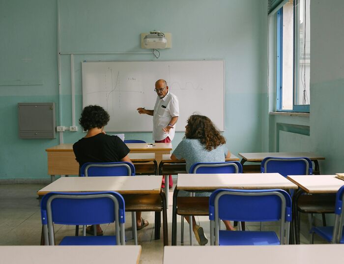 Teacher explaining a lesson on a whiteboard to two students in a classroom, illustrating arrogant people interacting.