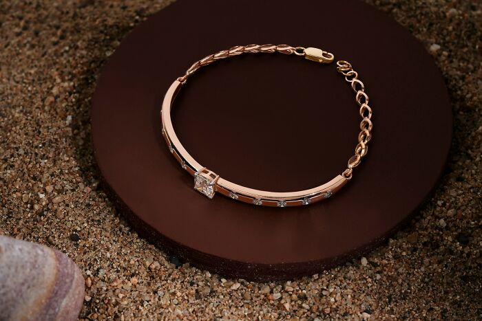 Rose gold bracelet with a central diamond placed on a brown circular platform on a sandy surface, illustrating bizarre beliefs. - 15