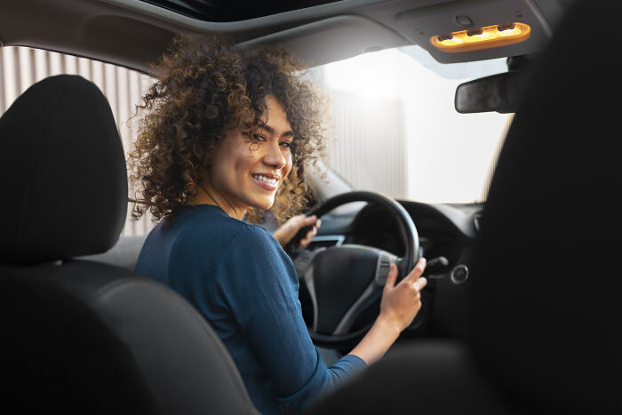 Woman smiling while driving a car, representing oddly specific green flags that indicate someone special in relationships.