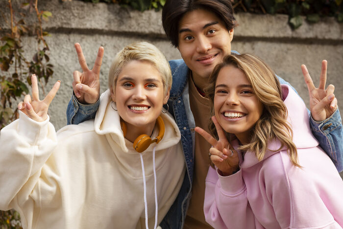 Three friends smiling and making peace signs outdoors, representing positive green flags in relationships and friendships.