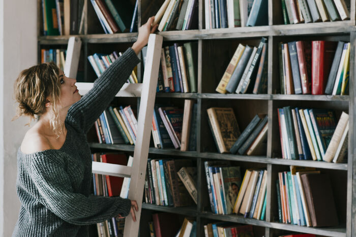 Woman reaching for a book on a tall bookshelf, symbolizing finding specific green flags in someone special.