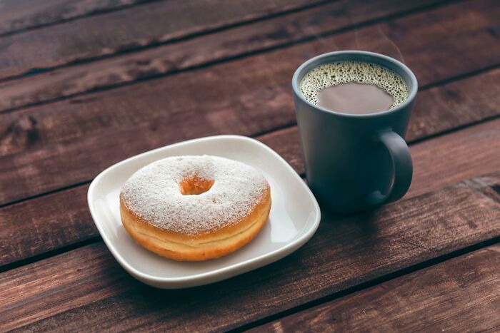 Powdered doughnut on a white plate next to a steaming cup of coffee on a wooden table, representing green flags.