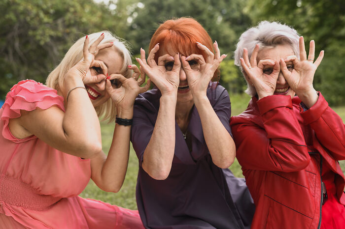 Three women outdoors making hand gestures over their eyes, representing green flags in relationships and connection.