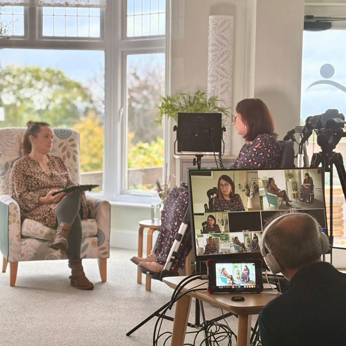 Support group session filmed indoors, two women talking, camera crew recording, addressing woman who ended life by starving.